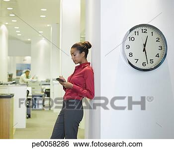 Stock Photo - businesswoman 
in office using 
pda near a clock. 
fotosearch - search 
stock photos, 
pictures, images, 
and photo clipart
