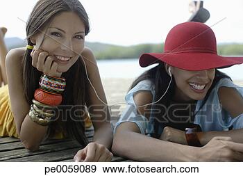 Arquivo Fotográficos - dois,  mulheres, 
 mentindo,  doca, 
 earbuds. fotosearch 
- busca de fotos, 
imagens e clipart