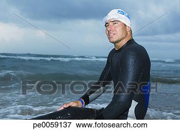 Picture - man in wet suit 
sitting on shore 
of beach. fotosearch 
- search stock 
photos, pictures, 
images, and photo 
clipart