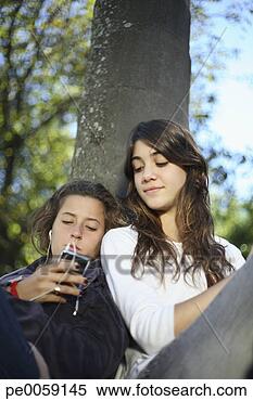 Stock Image - two girls leaning 
against a tree 
with an mp3 player. 
fotosearch - search 
stock photos, 
pictures, images, 
and photo clipart