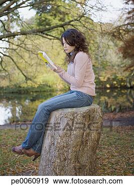 Arquivo Fotográficos - mulher,  sentando, 
 livro,  ao ar 
livre,  lago, 
 toco. fotosearch 
- busca de fotos, 
imagens e clipart