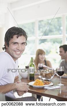 Stock Photo - man at a dinner 
table smiling 
with couple in 
background. fotosearch 
- search stock 
photos, pictures, 
images, and photo 
clipart