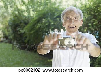 Stock Photo - senior man outdoors 
holding out digital 
camera and smiling. 
fotosearch - search 
stock photos, 
pictures, images, 
and photo clipart