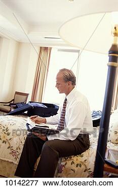 Picture - businessman reviews 
schedule in hotel 
room sitting on 
hotel bed. fotosearch 
- search stock 
photos, pictures, 
images, and photo 
clipart