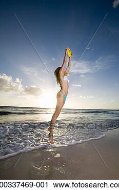 Stock Photography - young woman jumping 
to catch flying 
disc on beach, 
side view. fotosearch 
- search stock 
photos, pictures, 
images, and photo 
clipart