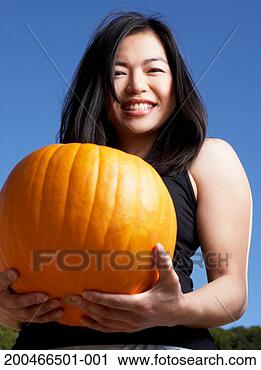 Stock Photography - young woman carrying 
pumpkin, portrait, 
low angle view. 
fotosearch - search 
stock photos, 
pictures, images, 
and photo clipart