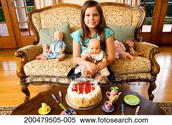 Stock Image - girl (7-9) sitting 
on sofa with dolls 
and cake, smiling, 
portrait. fotosearch 
- search stock 
photos, pictures, 
images, and photo 
clipart