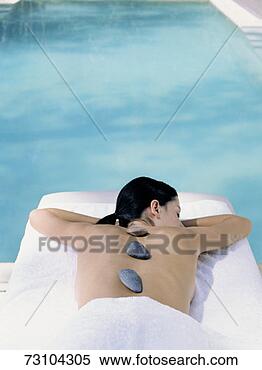 Stock Image - woman lying by 
pool, rocks lined 
up along spine, 
elevated view. 
fotosearch - search 
stock photos, 
pictures, images, 
and photo clipart