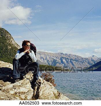 Stock Photo - young man sitting 
on rock beside 
lake, resting 
chin on hand. 
fotosearch - search 
stock photos, 
pictures, images, 
and photo clipart