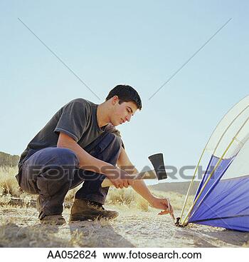 Stock Photo - young man using 
hatchet to pound 
tent peg into 
ground, side view. 
fotosearch - search 
stock photos, 
pictures, images, 
and photo clipart