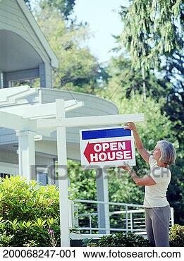 Stock Photography - mature woman hanging 
open house sign 
in front of house. 
fotosearch - search 
stock photos, 
pictures, images, 
and photo clipart