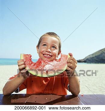 Stock Photography - boy (6-8) holding 
slice on watermelon 
on beach, smiling. 
fotosearch - search 
stock photos, 
pictures, images, 
and photo clipart