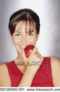 Stock Photography - young woman holding 
apple to mouth, 
smiling, portrait. 
fotosearch - search 
stock photos, 
pictures, images, 
and photo clipart