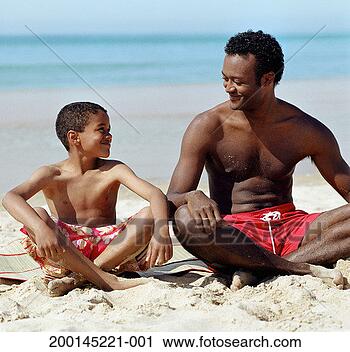 Stock Photography - man and boy (7-9) 
sitting cross 
legged on beach, 
smiling. fotosearch 
- search stock 
photos, pictures, 
images, and photo 
clipart