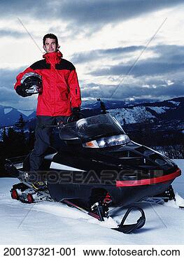 Stock Photography - young man standing 
on snowmobile, 
holding helmet, 
portrait. fotosearch 
- search stock 
photos, pictures, 
images, and photo 
clipart
