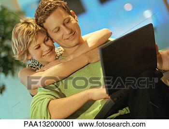 Stock Photography - couple smiling, 
man using laptop, 
woman with arms 
around man. fotosearch 
- search stock 
photos, pictures, 
images, and photo 
clipart