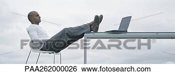 Stock Photo - man sitting outdoors 
with feet up on 
table and laptop 
on table. fotosearch 
- search stock 
photos, pictures, 
images, and photo 
clipart