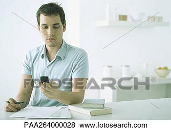 Stock Photo - young man at table 
with paper and 
books, looking 
down at cell phone. 
fotosearch - search 
stock photos, 
pictures, images, 
and photo clipart