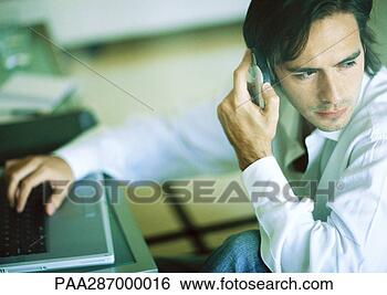 Stock Photo - man using laptop 
and cellphone, 
looking over shoulder. 
fotosearch - search 
stock photos, 
pictures, images, 
and photo clipart