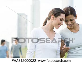 Stock Photo - two young women 
looking down at 
cell phone in 
urban park. fotosearch 
- search stock 
photos, pictures, 
images, and photo 
clipart