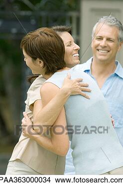 Stock Photo - two mature women 
hugging while 
man smiles in 
background. fotosearch 
- search stock 
photos, pictures, 
images, and photo 
clipart
