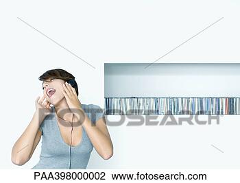 Stock Photo - woman listening 
to headphones, 
shelf of cds in 
background. fotosearch 
- search stock 
photos, pictures, 
images, and photo 
clipart