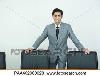 Stock Photo - businessman standing 
with hands on 
backs of chairs, 
 smiling at. fotosearch 
- search stock 
photos, pictures, 
images, and photo 
clipart