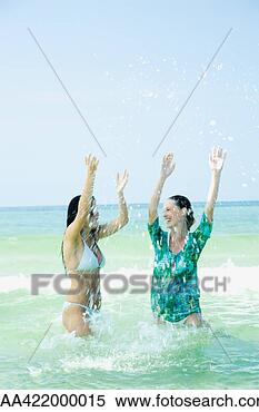 Stock Image - two young women 
standing waist 
deep in sea, splashing. 
fotosearch - search 
stock photos, 
pictures, images, 
and photo clipart