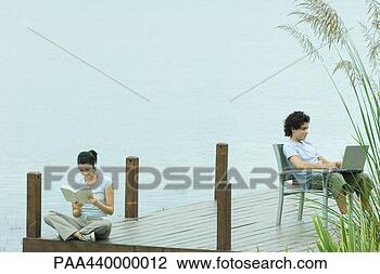 Banco de Imagem - par,  sentando, 
 doca,  leitura, 
 usando,  laptop. 
fotosearch - busca 
de fotos, imagens 
e clipart