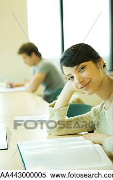 Stock Image - female college 
student sitting 
at table with 
book, smiling 
at camera. fotosearch 
- search stock 
photos, pictures, 
images, and photo 
clipart