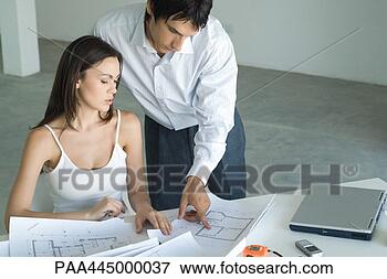 Picture - woman sitting 
at table looking 
at blueprints, 
 man standing, 
 looking. fotosearch 
- search stock 
photos, pictures, 
images, and photo 
clipart