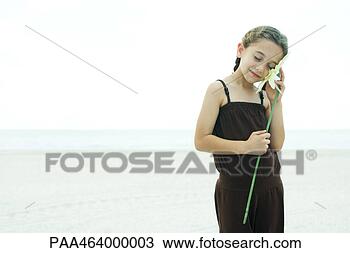 Stock Photo - girl standing 
on beach,  holding 
flower up to cheek, 
 eyes closed. 
fotosearch - search 
stock photos, 
pictures, images, 
and photo clipart