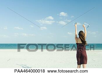 Stock Photo - woman standing 
on beach, holding 
up clear container, 
rear view. fotosearch 
- search stock 
photos, pictures, 
images, and photo 
clipart