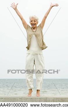 Stock Photography - senior woman standing 
on tiptoe at the 
beach, arms raised, 
smiling. fotosearch 
- search stock 
photos, pictures, 
images, and photo 
clipart