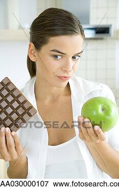 Picture - young woman holding 
apple in one hand 
and large bar 
of chocolate in. 
fotosearch - search 
stock photos, 
pictures, images, 
and photo clipart