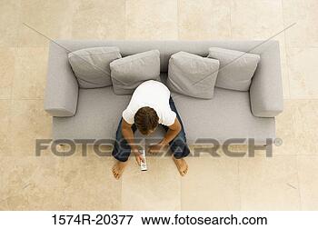 Picture - high angle view 
of a young man 
sitting on a couch 
with a remote. 
fotosearch - search 
stock photos, 
pictures, images, 
and photo clipart
