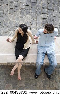 Stock Image - full length above 
view couple sitting 
on a bench on 
cobble stones. 
fotosearch - search 
stock photos, 
pictures, images, 
and photo clipart