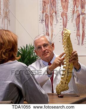 Stock Image - a chiropractor 
holding up a model 
of the human spine 
while talking 
to. fotosearch 
- search stock 
photos, pictures, 
images, and photo 
clipart
