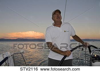 Stock Photo - a man at the helm 
of a sailboat 
at sunset. fotosearch 
- search stock 
photos, pictures, 
images, and photo 
clipart
