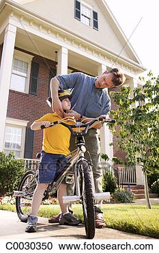 Stock Photography - low angle of a 
father fastening 
the straps to 
his son’s helmet 
before. fotosearch 
- search stock 
photos, pictures, 
images, and photo 
clipart