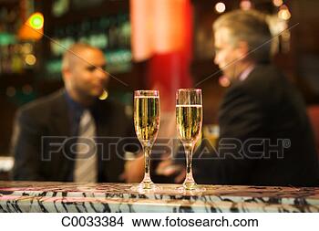 Stock Photo - two glasses of 
champagne sit 
on a bar in the 
foreground while 
two. fotosearch 
- search stock 
photos, pictures, 
images, and photo 
clipart