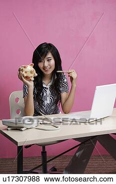 Banco de Imagem - jovem,  mulher, 
 segurando,  porca, 
 poupar,  sentando, 
 escrivaninha. 
fotosearch - busca 
de fotos, imagens 
e clipart