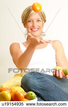 Stock Image - woman tossing 
orange, fruit 
bowl in foreground. 
fotosearch - search 
stock photos, 
pictures, images, 
and photo clipart