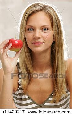 Foto - jovem,  mulher, 
 longo,  loura, 
 cabelo,  comer, 
 maçã,  retrato. 
fotosearch - busca 
de fotos, imagens 
e clipart