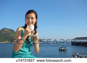 Foto - jovem,  senhora, 
 banco,  mar, 
 bebendo,  copo, 
 chá,  sorrindo. 
fotosearch - busca 
de fotos, imagens 
e clipart