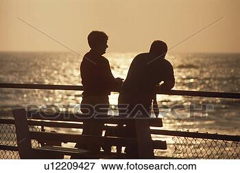 Foto - dois,  pessoas, 
 falando,  pôr 
do sol. fotosearch 
- busca de fotos, 
imagens e clipart