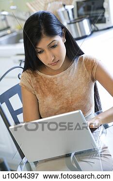 Picture - asian/indian young 
woman sitting 
at table working 
on laptop computer. 
fotosearch - search 
stock photos, 
pictures, images, 
and photo clipart