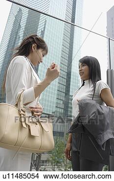 Stock Photo - a side view of 
two women shares 
a joke standing 
beside the glass. 
fotosearch - search 
stock photos, 
pictures, images, 
and photo clipart