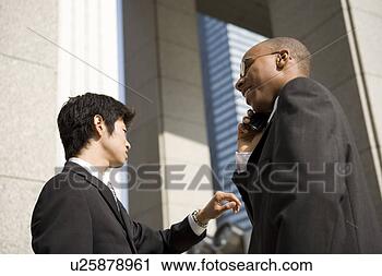 Stock Photography - two businessmen, 
one using mobile 
phone. fotosearch 
- search stock 
photos, pictures, 
images, and photo 
clipart