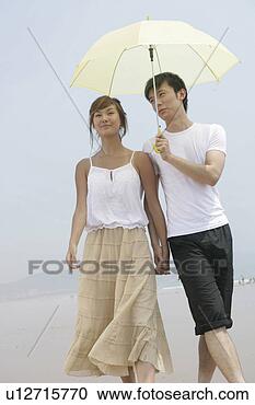 Stock Photography - young lovers under 
umbrella and walking 
on beach. fotosearch 
- search stock 
photos, pictures, 
images, and photo 
clipart